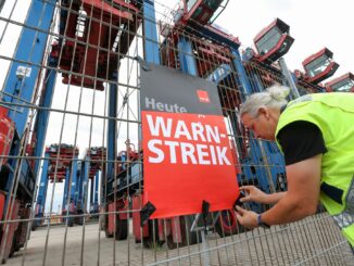 Ein Mann mit Warnweste bringt im Hamburger Hafen ein Plakat an.