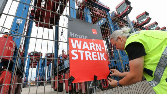 Ein Mann mit Warnweste bringt im Hamburger Hafen ein Plakat an.