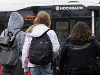 Zwei Schülerinnen und ein Schüler warten in Hamburg auf einen Bus. (Symbolbild)