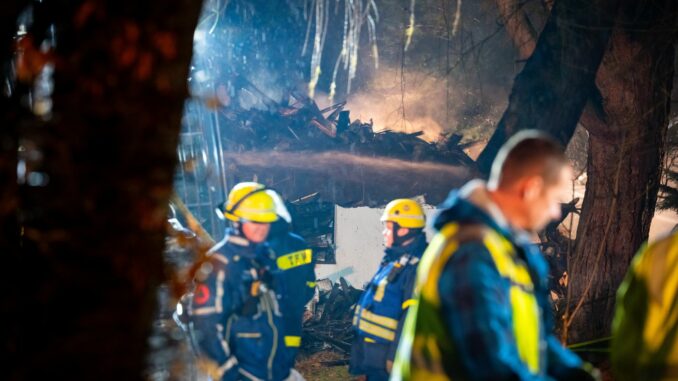 Reste des abgebrannten Hauses qualmen während den Nachlöscharbeiten hinter Einsatzkräften des THW.